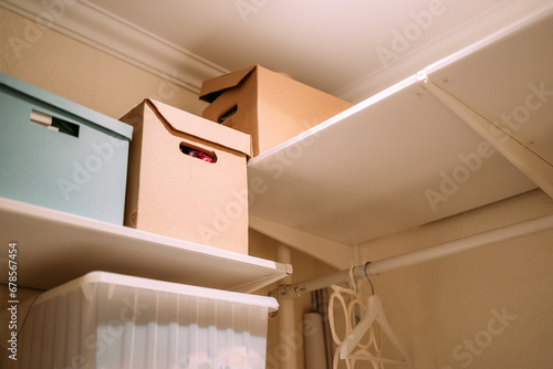 A pantry with white walls in the apartment, cardboard boxes for storing things, shelves, hangers