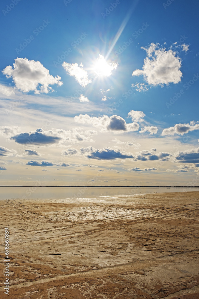 Scenic sunlight landscape, shore of salt lake with medicinal mud, water surface and reflections sky with clouds. Beautiful aesthetic nature view. Ulzhay (Uldjay) lake in Omsk region, Russia.