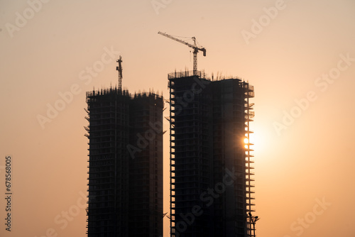 Silhouette of under construction building against sunset with crane on roof showing rapid real estate infrastructure growth in gurgaon delhi mumbai photo