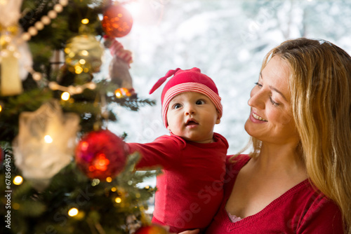 Little cute baby and his mother enjoying shiny lights and ornaments on the Christmas tree