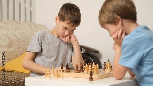 Two Caucasian boys are playing chess at home in living room. Older brother teaches younger one to play chess. Leisure game.