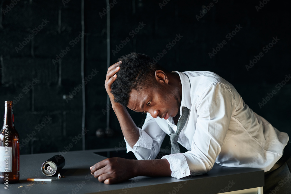 African American young man having problems with alcohol, he standing at table with bottles and cigarettes African American young man having problems with alcohol, he standing at table with bottles and cigarettes