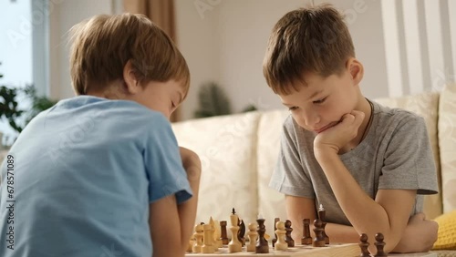 Two Caucasian boys are playing chess at home in living room. Older brother teaches younger one to play chess. Leisure game.