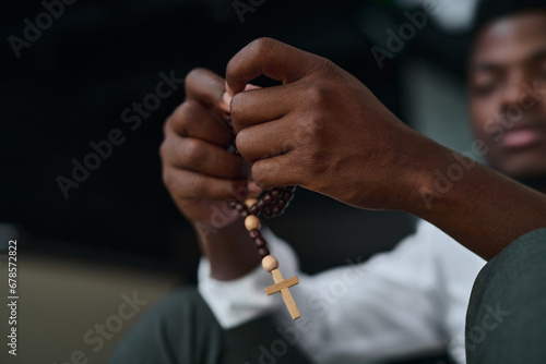 Close-up of African American man sitting with rosary beads and praying in difficult situation