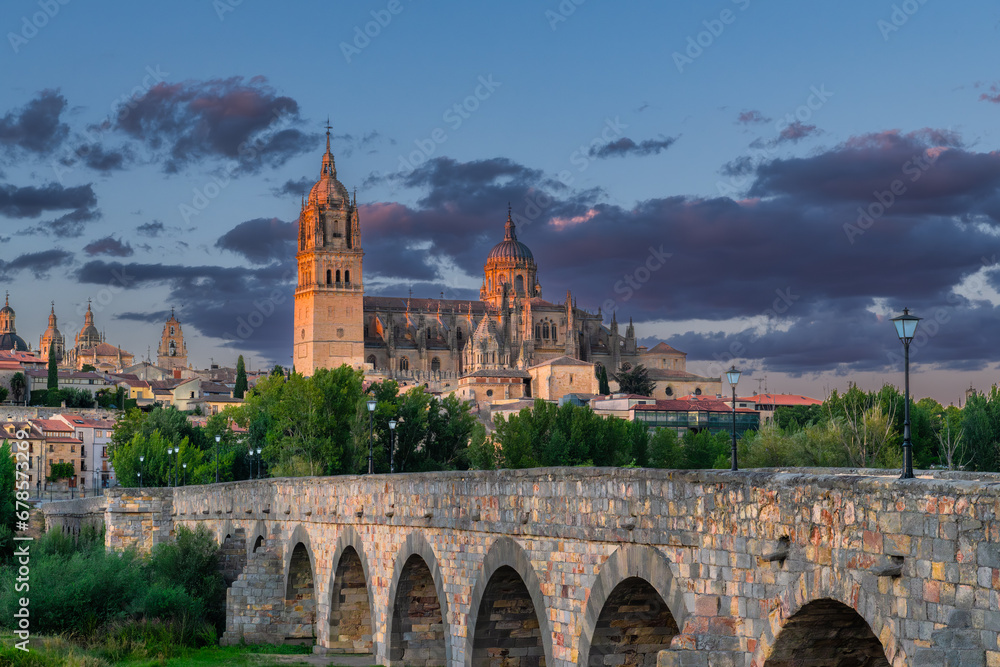 Sunset view of The Salamanca Roman Bridge (Puente Romano de Salamanca, Puente Mayor del Tormes), ancient stone structure over the Tormes River with Salamanca Cathedral in the background