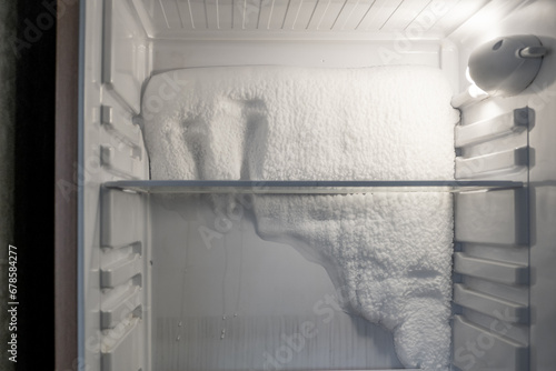 Frozen refrigerator that needs to be defrosted. Block of ice in the empty fridge. empty shelves in the refrigerator. Refrigerator maintenance.  photo