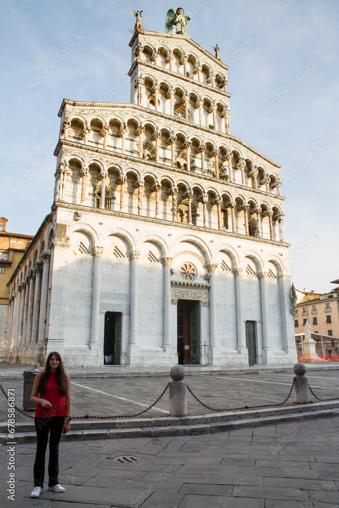 A young Caucasian woman in front of San Michele in Foro, a Roman Catholic basilica located in Lucca, Tuscany, Italy. The church is built in Romanesque style and is located in the historic center.