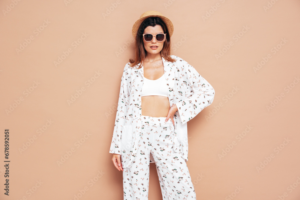 Young beautiful smiling female in trendy summer costume clothes. Carefree woman posing near beige wall in studio. Positive model having fun indoors. Cheerful and happy. In hat and sunglasses Young beautiful smiling female in trendy summer costume clothes. Carefree woman posing near beige wall in studio. Positive model having fun indoors. Cheerful and happy. In hat and sunglasses