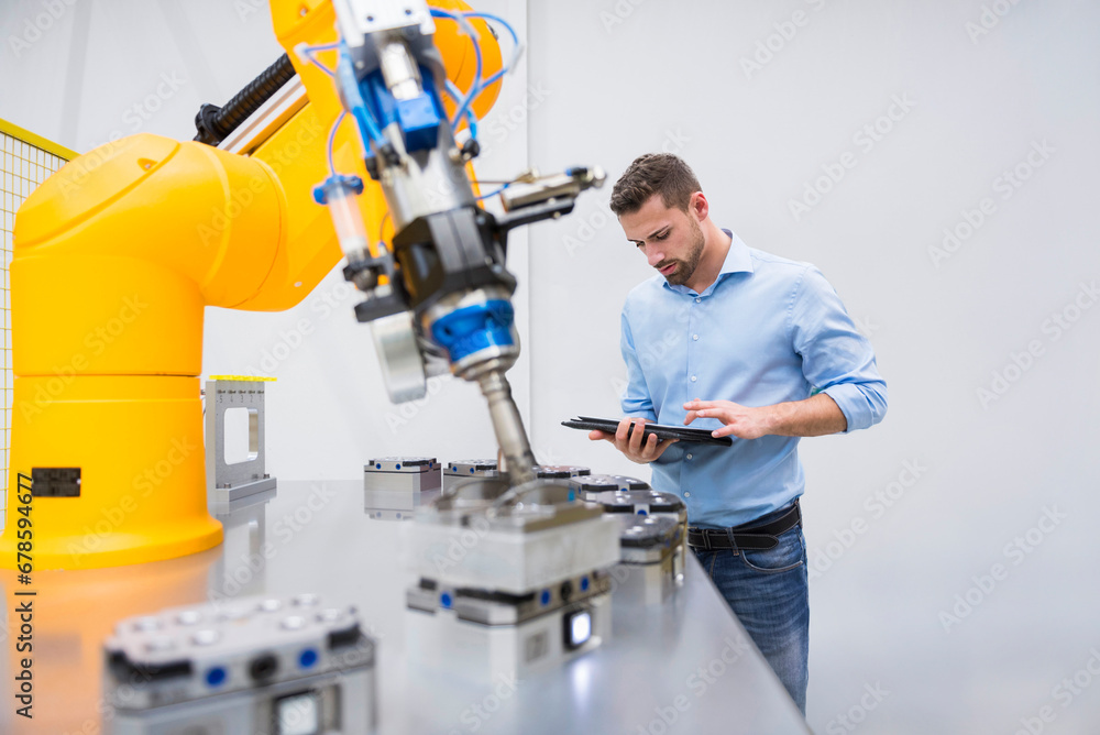 Engineer using tablet PC near robotic arm in factory Engineer using tablet PC near robotic arm in factory