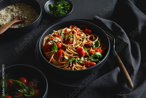 Bowl of vegan wholemeal spelt spaghetti with tomatoes, basil, scallion and cashew Parmesan