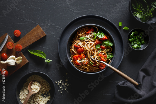 Bowl of vegan wholemeal spelt spaghetti with tomatoes, basil, scallion and cashew Parmesan photo