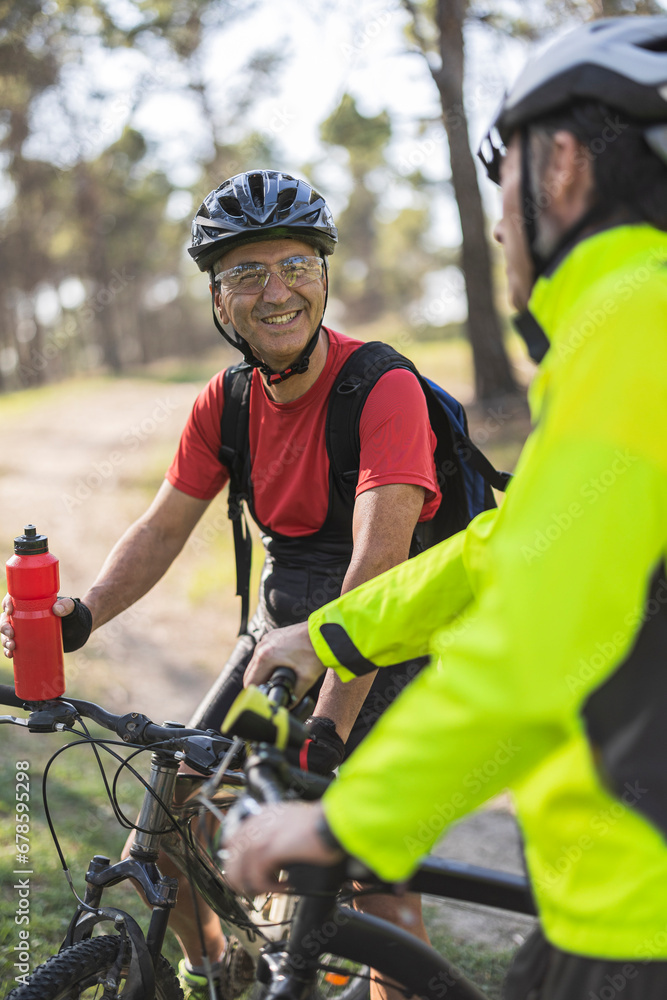 Smiling man holding water bottle and talking to friend in forest Smiling man holding water bottle and talking to friend in forest