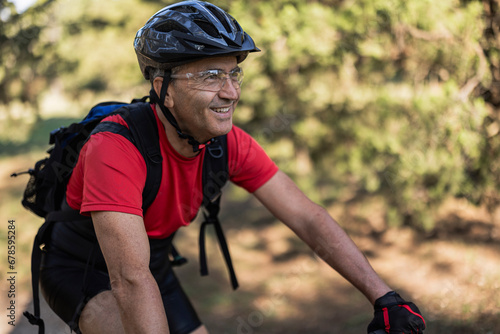 Smiling man wearing helmet and cycling in forest photo