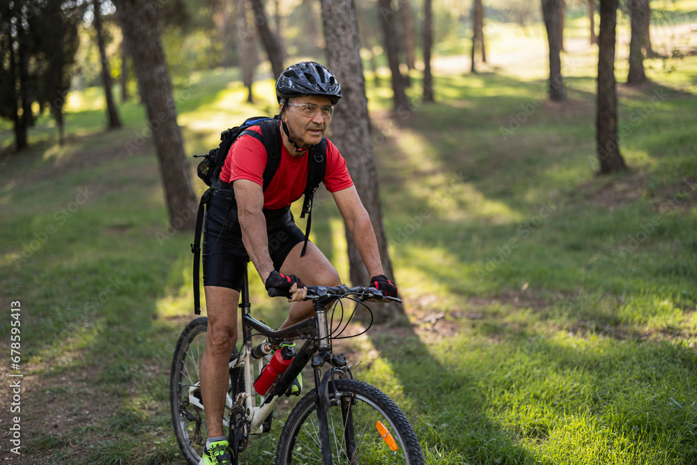 Mature man wearing helmet and riding bicycle in forest on sunny day Mature man wearing helmet and riding bicycle in forest on sunny day