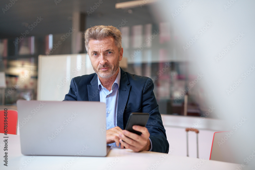 Smiling mature businessman sitting with mobile phone and laptop at table Smiling mature businessman sitting with mobile phone and laptop at table