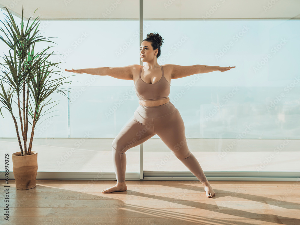 Smiling woman doing warrior pose near potted plant in yoga studio Smiling woman doing warrior pose near potted plant in yoga studio