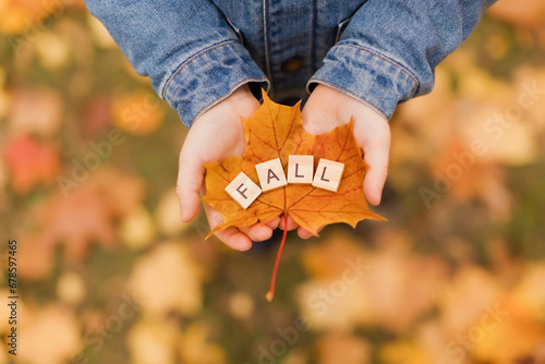 Boy holding wooden fall letters on leaf in hand at autumn park photo