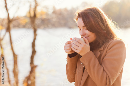 Smiling woman drinking tea from cup by lake at sunset photo