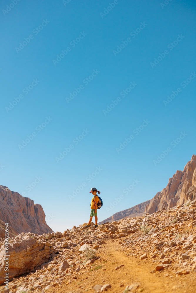 little boy with a backpack stands along the path against the backdrop of the mountains.  travel with children to the mountains. Turkey. Aladaglar.