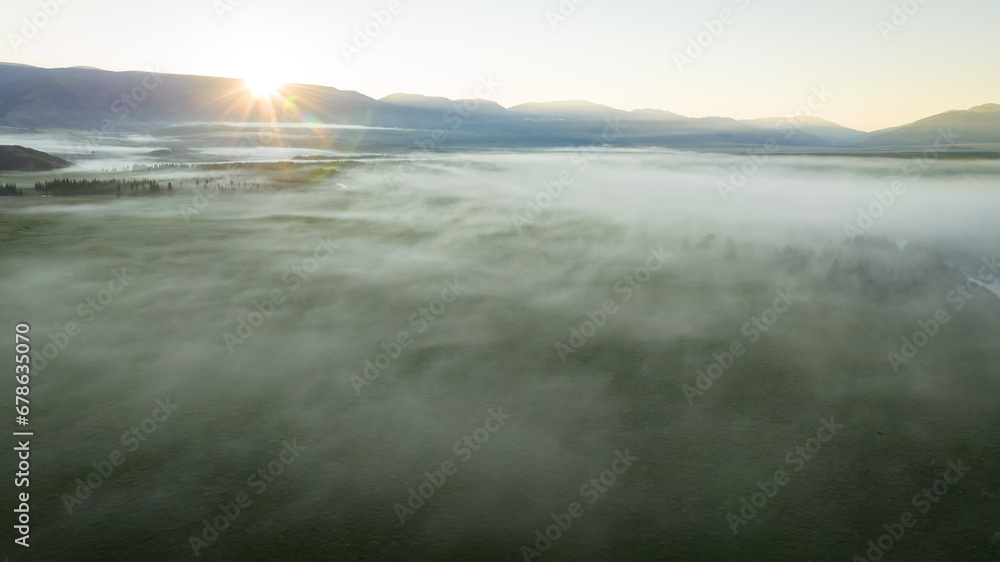 Obraz premium Early morning landscape. Foggy river. River valley in the morning fog at sunrise. View from above. Rays of the sun breaking through the fog in over the trees