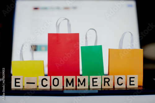 E-commerce and online shopping concept.  Laptop, colourful bags and wooden letters in the center. Blurred background.
