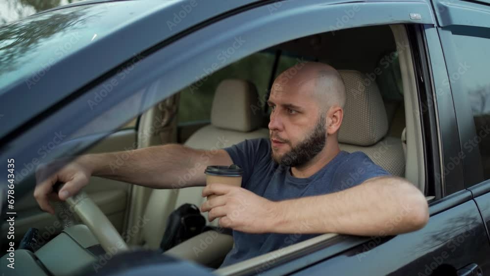 Bearded man driving a car while drinking takeaway coffee, view through window Bearded man driving a car while drinking takeaway coffee, view through window