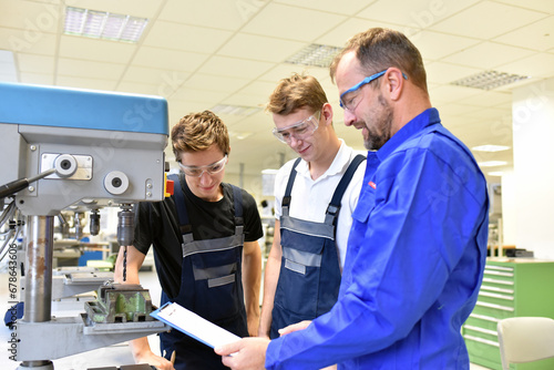trainer and apprentice in technical vocational training at a drilling machine