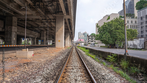 A railroad track with steel on both sides to allow trains to run. The floor is full of stones. On the side is a road and condos.