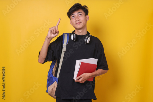 Asian male student holding books with cheerful expression pointing above photo