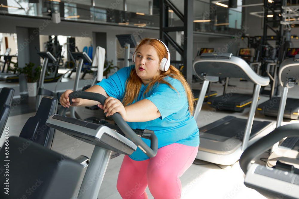 Fototapeta premium Tired young woman with obesity on treadmill during training workout
