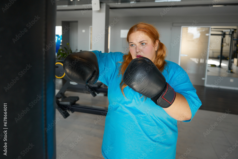 Concentrated fat woman using boxing gloves doing punching exercises