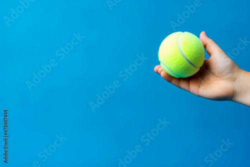 Partial view of sportive young woman holding tennis ball in her hand with blue background, close up shot of brand new tennis ball © VisualProduction