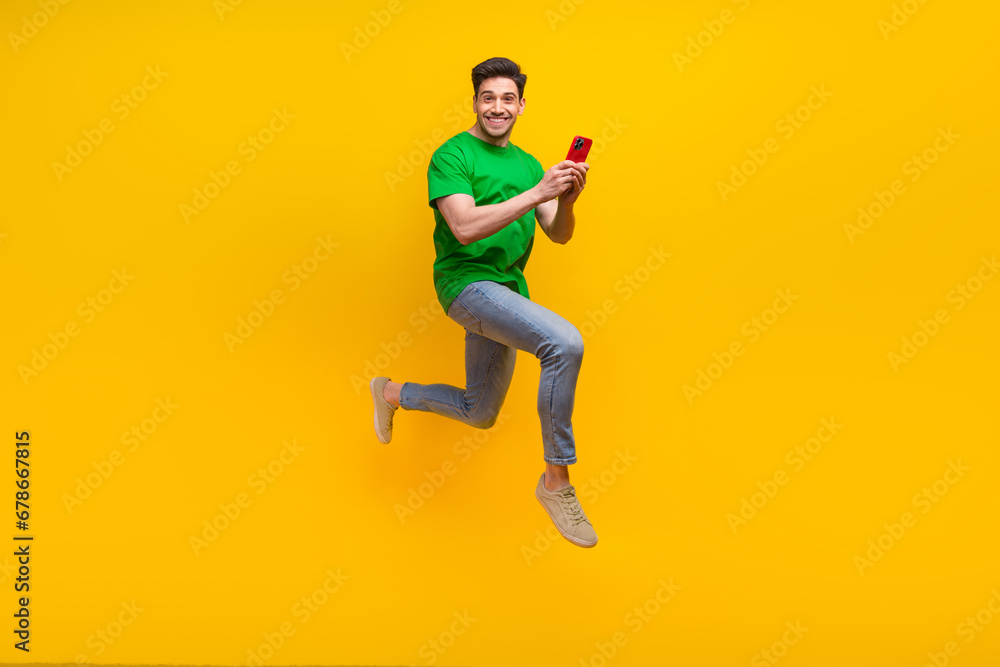 Full size photo of cool funny guy wear stylish t-shirt run to empty space with smartphone in hands isolated on yellow color background