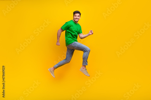 Full size photo of positive cheerful guy wear stylish t-shirt jumping run shopping to empty space isolated on yellow color background © deagreez