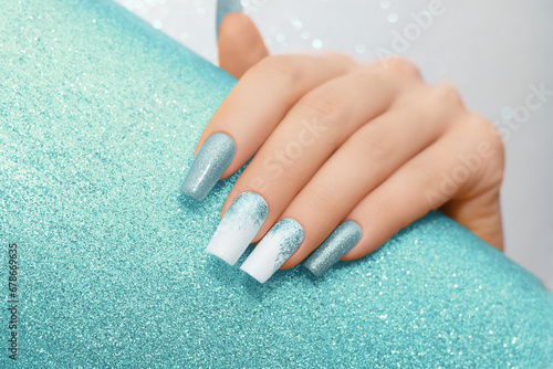 Female hand with long nails with glitter nail polish. Long blue nail design. Women hand with sparkle manicure on glitter background