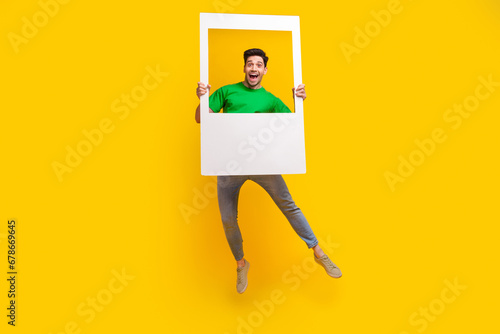 Full size photo of positive cheerful excited guy wear stylish t-shirt jumping posing in photo frame isolated on yellow color background