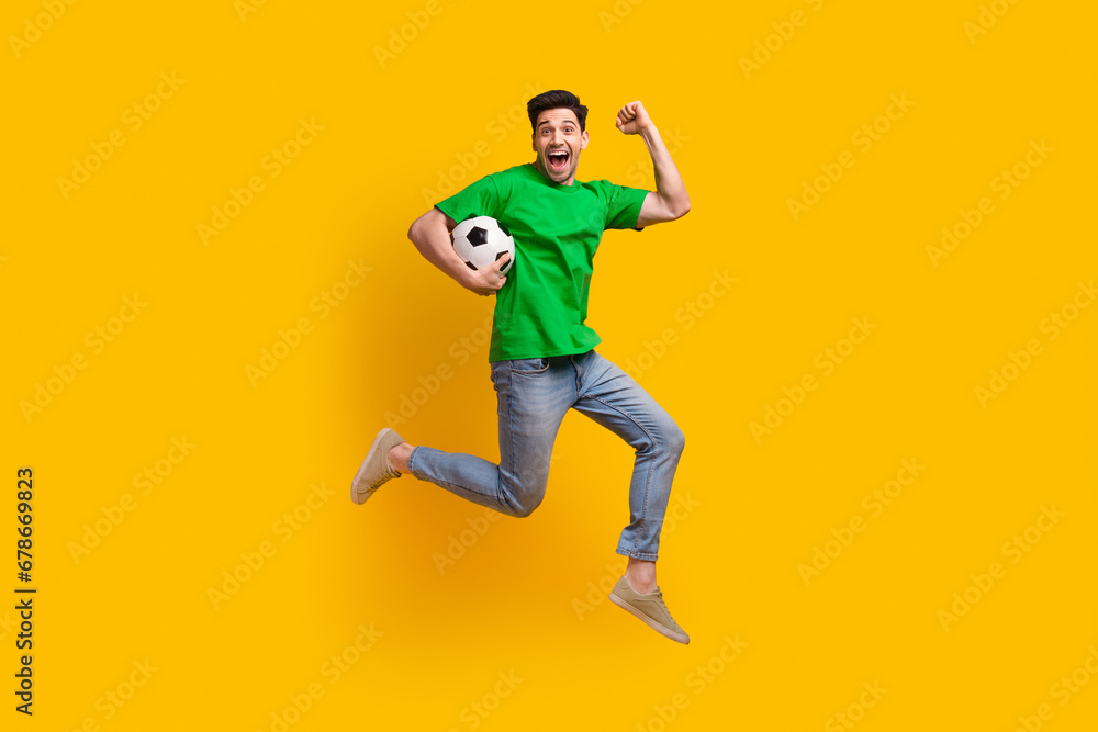 Full size photo of crazy guy wear stylish t-shirt jeans run with football ball in hand support team isolated on yellow color background