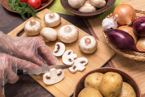 Chef cutting, slicing cooking mushrooms champignon and red onion close up. Hands in gloves cooking vegetarian vegetables dish