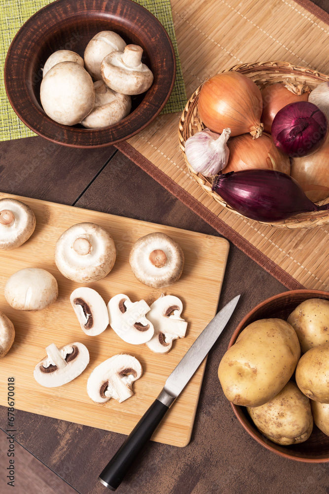 Sliced mushrooms champignon on wooden cutting board with onion garlic and potato on kitchen. Cooking vegetarian vegan food