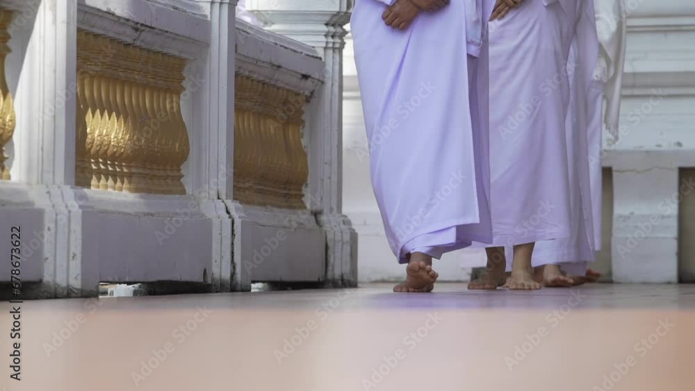 The legs of a Buddhist nun or female meditator wearing white cloth walk in a line to meditate in a temple. The legs of a Buddhist nun or female meditator wearing white cloth walk in a line to meditate in a temple.