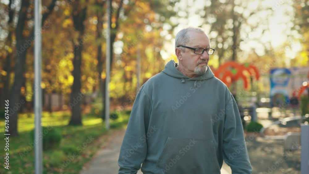 An elderly man of retirement age wearing glasses is walking in a park and looking around. Pensioner in the park An elderly man of retirement age wearing glasses is walking in a park and looking around. Pensioner in the park