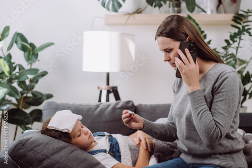Sad sick preteen kid girl lying on sofa feel fever catch cold flu influenza. Anxious mom holding phone to ear make call to doc family therapist after measuring child temperature. Calling family doctor