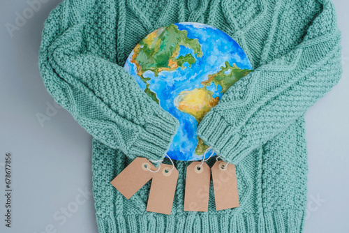 Sleeves of knitwear sweater hug the planet with tags. Responsible consumption clothes. Environmental friendliness and sustainable fashion. Zero waste