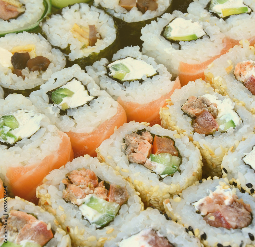 Close-up of a lot of sushi rolls with different fillings lie on a wooden surface. Macro shot of cooked classic Japanese food with a copy space. Close-up of a lot of sushi rolls with different fillings lie on a wooden surface. Macro shot of cooked classic Japanese food with a copy space.
