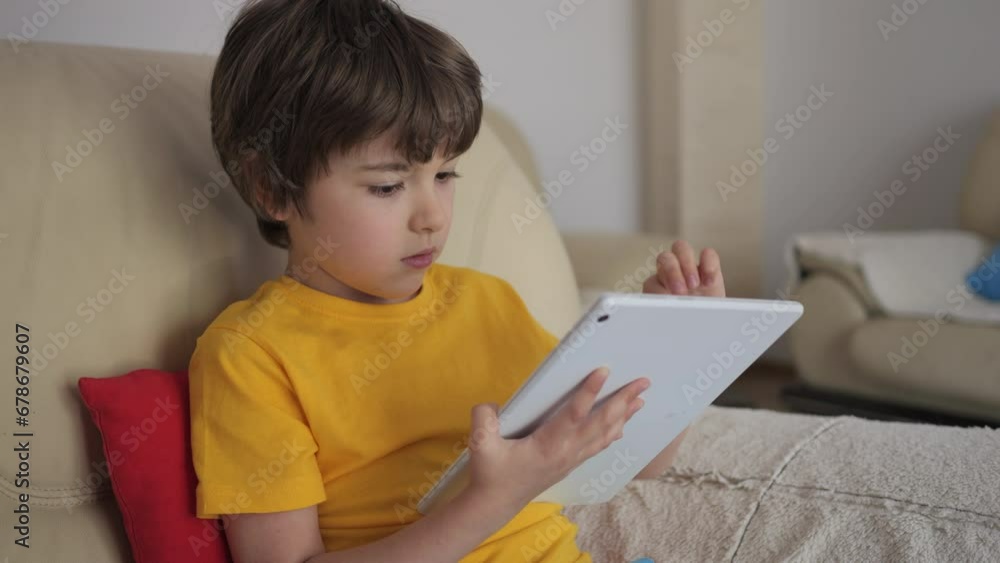 Portrait of Cute Boy Playing Game on Tablet PC Relaxing in Living Room. Child Browsing Social Media. Child Using Tablet PC Sitting on Sofa at Home, Homeschooling, Distant Remote Education. Portrait of Cute Boy Playing Game on Tablet PC Relaxing in Living Room. Child Browsing Social Media. Child Using Tablet PC Sitting on Sofa at Home, Homeschooling, Distant Remote Education.