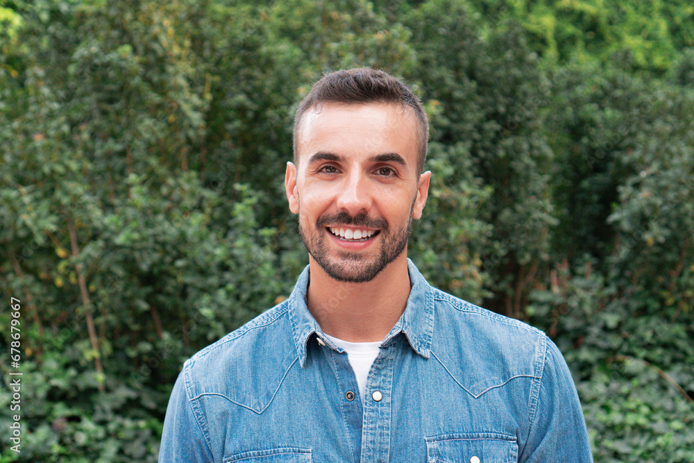 Young male isolated looking at camera and smilinig. A happy man portrait outdoor with green and natural background Young male isolated looking at camera and smilinig. A happy man portrait outdoor with green and natural background