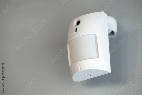 Billede på lærred A white motion sensor camera on a gray wall, providing security and surveillance