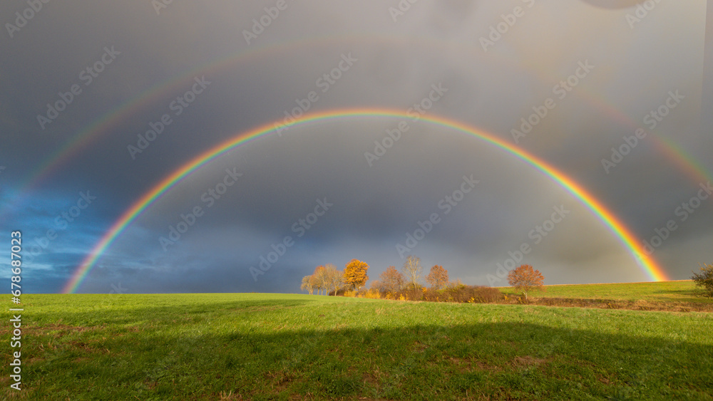 Fototapeta premium Ein Regenbogen über einer Landschaft mit Wiesen und Bäumen