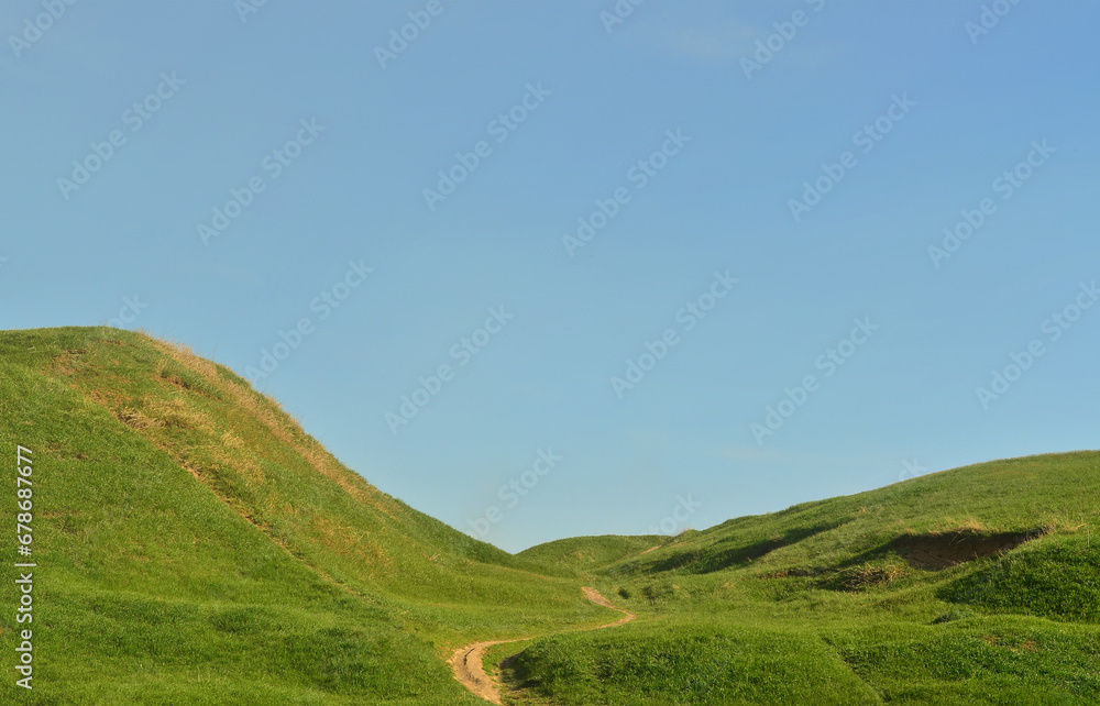 Fototapeta premium Landscape with a trampled path, passing through a wonderful green mountainous terrain. Photo of beautiful landscaped relief space with a thin path