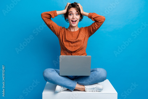 Full body photo of pretty young girl touch head astonished netbook eshop dressed stylish brown outfit isolated on blue color background © deagreez
